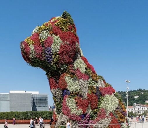 A giant dog-shaped covered in colourful living flowers installed outdoors in a public plaza