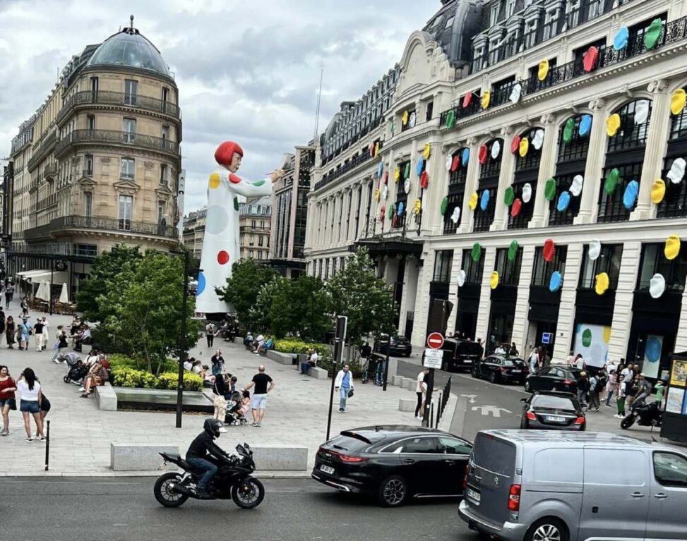 Provide: Title: creating infinity Artist/creator: Kusama Location: Paris France Date: July 2023 Part 1: Visual Description (Approx. 250 words) Include: Visual elements (line, color, space, scale, texture) Composition and focal point Materials or medium This image shows a large building covered in brightly coloured randomly placed polka dots, that go up three quarters of the building in height and around half the width of the building, wrapping around the corner. The polka dots end in the middle of the building where you are met with a giant statue of artist Yayoi Kasuma, who made this piece. This is a huge sculpture, standing around 50 feet in height, being almost as tall as the building the polka dots are on. The sculpture is holding a paintbrush, shown to be in the middle of painting and covering the building in polka dots. The giant sculpture of Kasuma is wearing a white dress with polka dots matching the building. The colours in this piece are bright, vibrant green, blue, yellow, red and white. These colours pop boldly against the plain cream and black colours of the building. The artist uses many different materials to make this piece, as there are many different components. For the polka dots on the building, she uses lots of vinyl as it’s available in the bright colours Kasuma gravitates to. Vinyl is also available in large quantities, making it easier for large scale installations. For the sculpture aspect, she uses more carbon fiber, fiber glass and acrylic paints. Because this installation is on a Louis Vuitton building along a popular high end shopping strip in Paris, it will have a high amount of viewers. Section 2: Interpretation & Meaning (Approx. 300–350 words) Interpret the work using evidence from your description. Address: Possible ideas or messages communicated How the space shapes meaning and audience experience How different viewers might interpret the work differently The brightly coloured polka dots encourage playfulness and the use of your imagination. The large scale of both the erratically placed polka dots covering the building and the statue, along with the vibrant colours post a great contrast with the dull tones and symmetry of the surrounding buildings to this piece. The colourful dots across the building resemble confetti or sprinkles, resulting in a youthful feeling. Hinting at joy and spontaneousness. By placing a piece this large and playful in a public place with formal architecture, it allows for the public to critically think about how art should look in traditional settings. The meaning behind this piece is heavily shaped on where it is located. By being placed in the middle of a busy shopping strip, surrounded by cafes, pedestrians and museums, this artwork gets incorporated into everyday life rather than an isolated piece in a formal setting. This piece gets viewed as people pass through this space. Which can increase the surprise and curiosity of stumbling upon this art. The scale of the statue along with the polka dots scaling most of the height of the building forces viewers to stop and look up to ensure the full experience of this art. By having the bright dots cover the majority of the building\'s length, it transforms the traditional plain architecture of the block into an immersive experience instead of just a single view point. There are multiple different ways this artwork could be interpreted by its viewers. Depending on the age and background of the viewers, everyone could interpret this differently. One way someone could experience this installation as uplifting and joyful, or reminiscent of childhood. While on the other hand, people may view the bright vibrancy as out of place against the muted tones of the historic architecture of the surrounding buildings. Seeing the work as a clash. Some could see the female figure symbolically, seeing power and freedom in a public space. Whereas children may not think as deeply, focusing on the colours instead. Observing this piece as playful and fun. These different meanings emphasize how public art allows for everyone to interpret art differently rather than a single message. Section 3: Space, Power, and Access (Approx. 150–200 words) Critically reflect on: Who encounters the work and who does not Who controls or owns the space Whether the encounter is planned or accidental Kasuma’s Creating Infinity is both a collaboration with Louis Vuitton and a large-scale public art installation in rue du Pont Neuf which is the Louis Vuitton headquarters in Paris. The piece was up from early to middle 2023, with the pictures above being from July 2023. The rue du Pont Neuf is a popular area for high end shopping. It is also close to the Louver, making it a high traffic area. Allowing for intentional and accidental encounters with this artwork. As a public art installation, this work is extremely accessible. Viewing this work doesn’t require you to pay an admission fee or a formal entry as you would in any museum or art gallery. Although, people who do not live or work by or visit the rue de Pont Neuf may never see this artpiece. Even though this work is on a grand scale many people could walk or drive right past never thinking about the piece, where others may stop and take time to look at this art and think deeper.