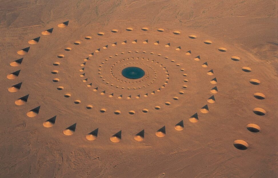 Aerial view of a circular sand formation with repeating rings of mounds and holes in a desert.
