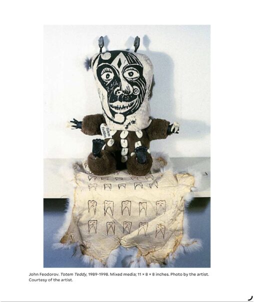 A teddybear with a stylized black and white mask like visage is seated on a patterned hide with tooth motifs in this mixed media artwork that combines toy form with iconography inspired by indigenous culture.